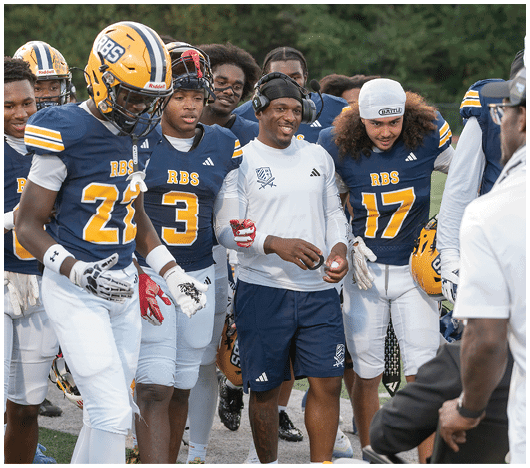 A group of people wearing blue and white football uniforms and helmets are gathered together outdoors, some smiling and interacting with each other. Description generated by AI