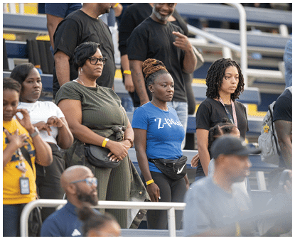 A group of people standing in a stadium with some wearing casual clothing and looking forward attentively. Description generated by AI