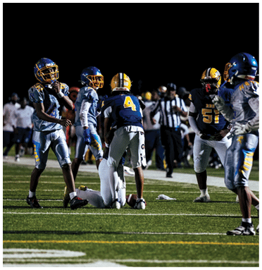 People wearing football uniforms are gathered on a field at night with a referee in the background. Description generated by AI