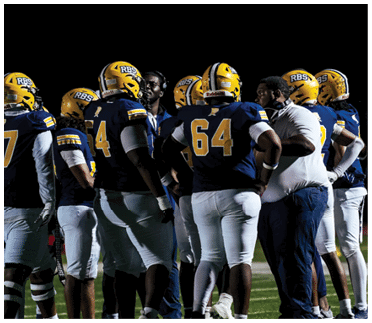 A group of people wearing yellow helmets with RBS logos are gathered closely together against a black background. Description generated by AI