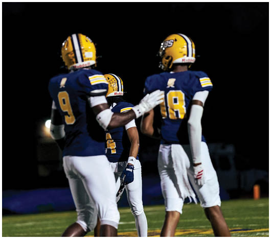 Two people wearing yellow football helmets with black and white stripes are standing against a dark night sky. Description generated by AI