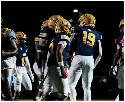 Several people wearing yellow helmets and blue and white football uniforms are gathered on a field at night. Description generated by AI