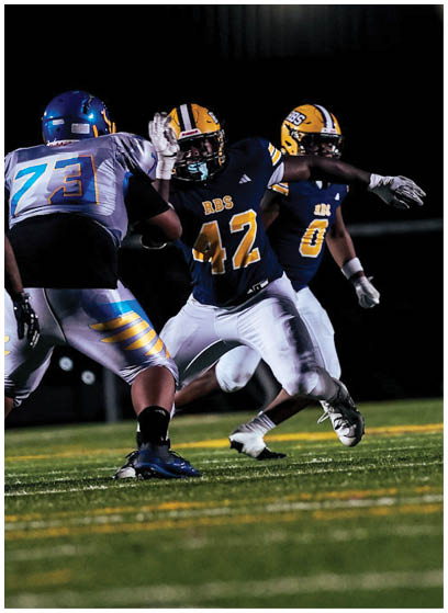People wearing football uniforms are engaged in a game on a grassy field under stadium lights. Description generated by AI