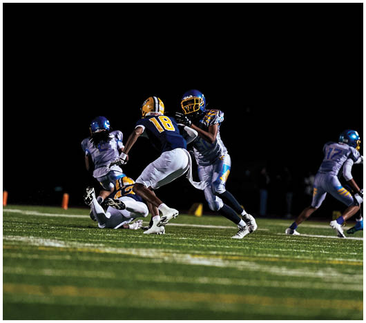 Several people in football uniforms are actively engaged in a nighttime game on a grassy field. Description generated by AI