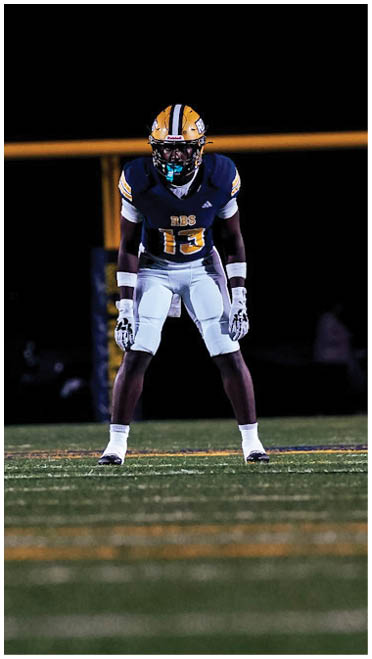Two people in football uniforms stand on a field under stadium lights with a goalpost in the background. Description generated by AI