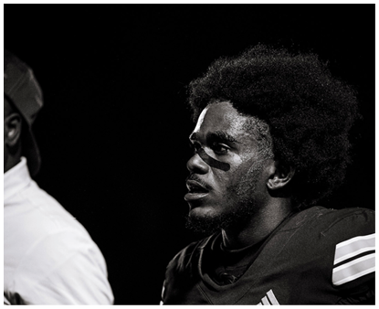 Two people in football gear are positioned on a field at night with blurred figures in the background. Description generated by AI