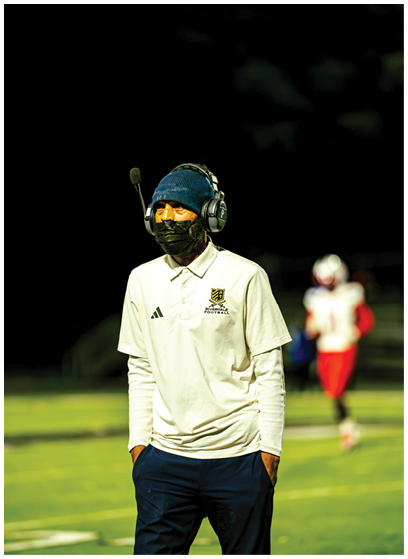 A person wearing a blue and yellow football uniform sits on a bench on a sports field with a helmet placed nearby. Description generated by AI