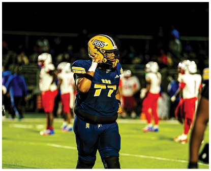 Two people in football gear are positioned on a field at night with blurred figures in the background. Description generated by AI