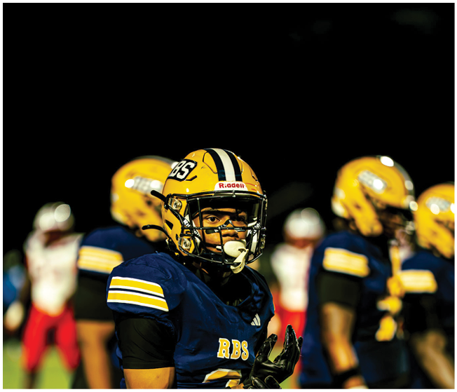 A group of people wearing football helmets and uniforms are gathered on a field under a dark night sky with a bright moon visible above. Description generated by AI