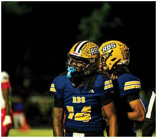 Two people wearing yellow football helmets with black and white stripes are standing against a dark night sky. Description generated by AI