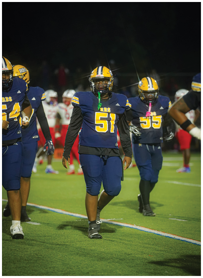 People wearing blue and yellow football uniforms are walking on a football field at night. Description generated by AI