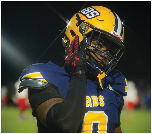 A person wearing a blue and yellow football uniform with the number zero is adjusting their helmet on a field at night. Description generated by AI
