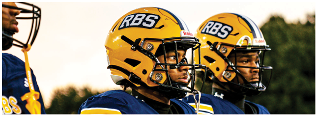 Two people wearing yellow helmets and blue football uniforms stand side by side, looking focused. Description generated by AI