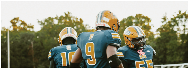 Three people wearing football helmets and jerseys are standing outdoors with trees in the background. Description generated by AI