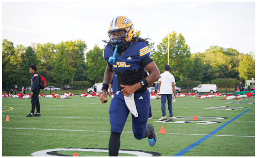 A person wearing a yellow and blue football helmet and uniform is standing outdoors under a partly cloudy sky. Description generated by AI