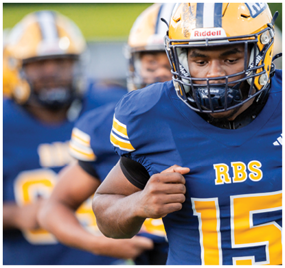An adult wearing a blue and yellow football uniform with the number 15 and the letters RBS is running on a field with other players in the background. Description generated by AI