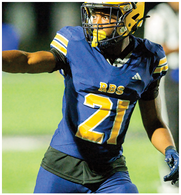 A person wearing a blue and yellow football uniform with the number 21 is on a field giving a thumbs-up gesture. Description generated by AI