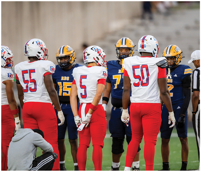A group of people wearing football helmets and uniforms are gathered on a field under a dark night sky with a bright moon visible above. Description generated by AI