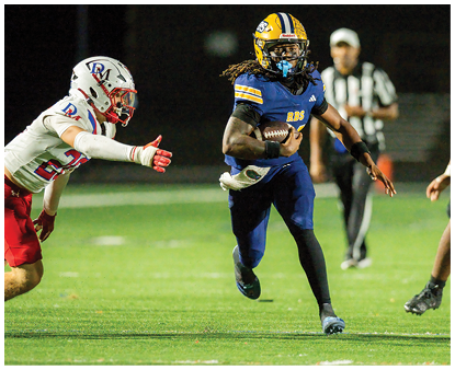 Two people in football gear are positioned on a field at night with blurred figures in the background. Description generated by AI