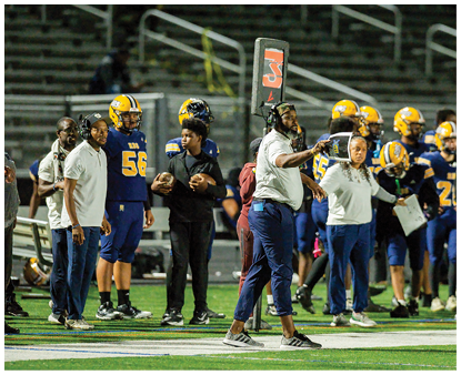 Two people in football gear are positioned on a field at night with blurred figures in the background. Description generated by AI