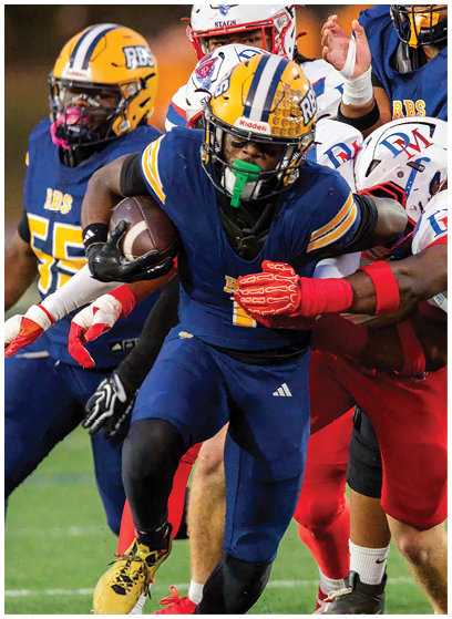 A person wearing a blue and yellow football uniform sits on a bench on a sports field with a helmet placed nearby. Description generated by AI