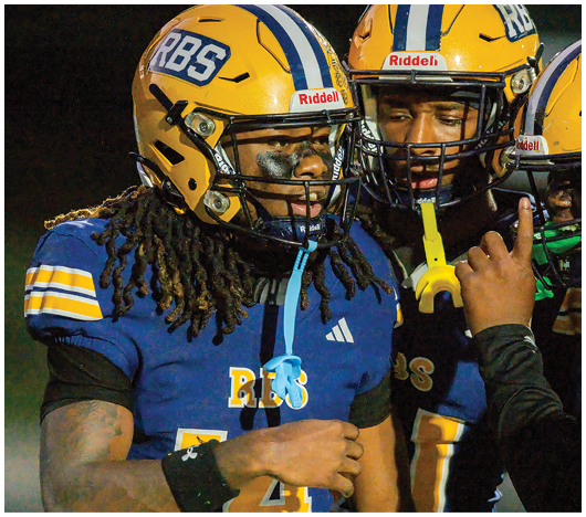 Two people wearing yellow football helmets with black and white stripes are standing against a dark night sky. Description generated by AI