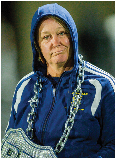 A person wearing a blue and yellow football uniform sits on a bench on a sports field with a helmet placed nearby. Description generated by AI