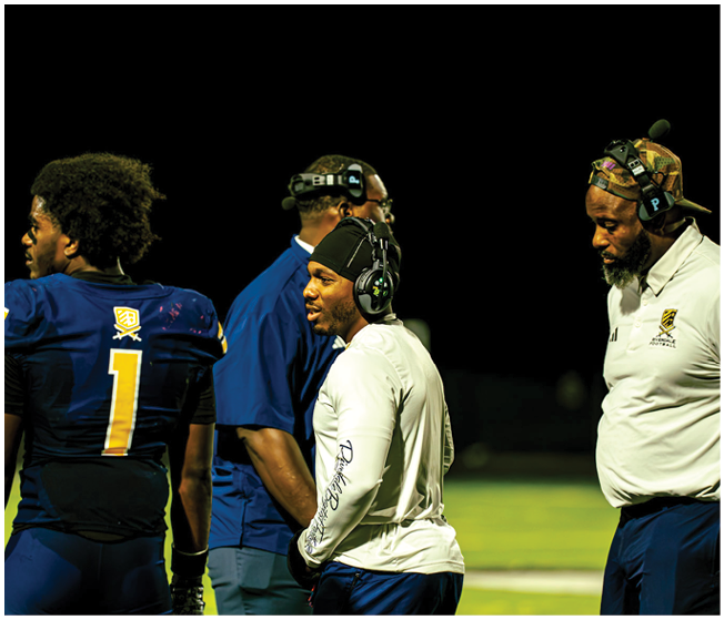A group of people wearing football helmets and uniforms are gathered on a field under a dark night sky with a bright moon visible above. Description generated by AI