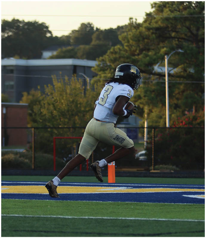 Three football players in blue and white uniforms running on a field. Description generated by AI