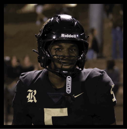 Two people wearing football uniforms and headsets are smiling and fist bumping each other on a sports field. Description generated by AI