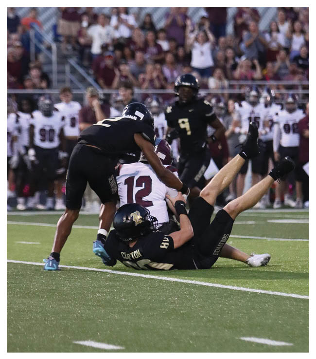 A football game is in progress with players on the field. One player is throwing a football while another player is trying to catch it. The players are wearing uniforms and are actively engaged in the game. AI generated content