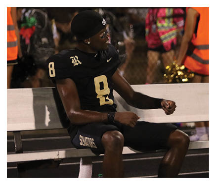 A man in a black jersey is running on a field with a football in his hand. AI generated content