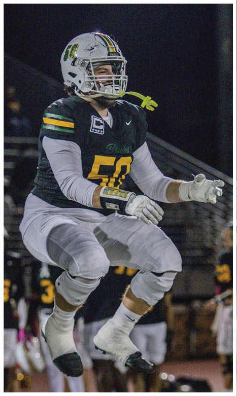 A person wearing a football uniform with a helmet and gloves is jumping on a field at night with other players blurred in the background. Description generated by AI
