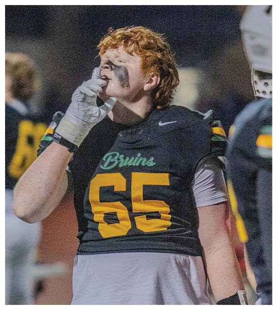 A person with curly hair wearing a football uniform with “Bruins" on the chest is drinking from a water bottle during a nighttime game. Description generated by AI