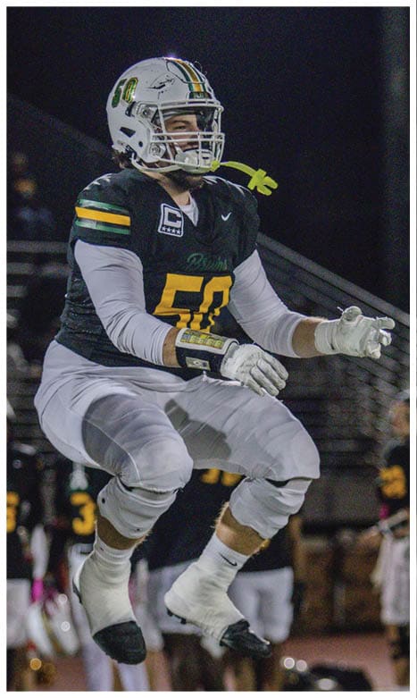 A person wearing a football uniform with a helmet and gloves is jumping on a field at night with other players blurred in the background. Description generated by AI