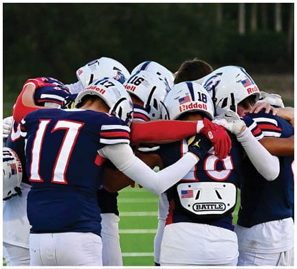 A group of football players huddled together on the field. Description generated by AI