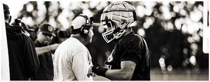 Two adults are engaged in a conversation on a sports field, with one wearing athletic gear and gloves. Description generated by AI
