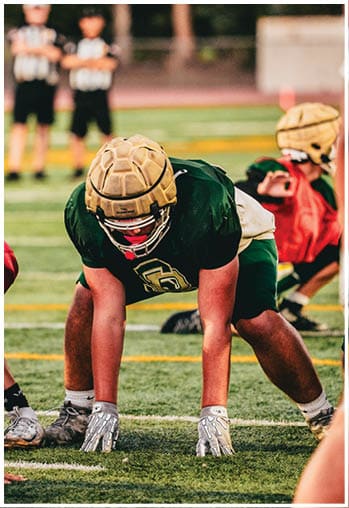 People in athletic gear are positioned on a football field in a ready stance, preparing for a play. Description generated by AI