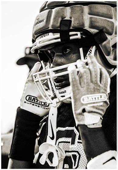 A person wearing a football helmet and gloves is holding a mouthguard near their face while looking intently ahead. Description generated by AI