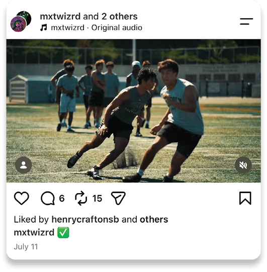 Two people in athletic clothing are running and competing on a sports field with several others standing in the background. Description generated by AI