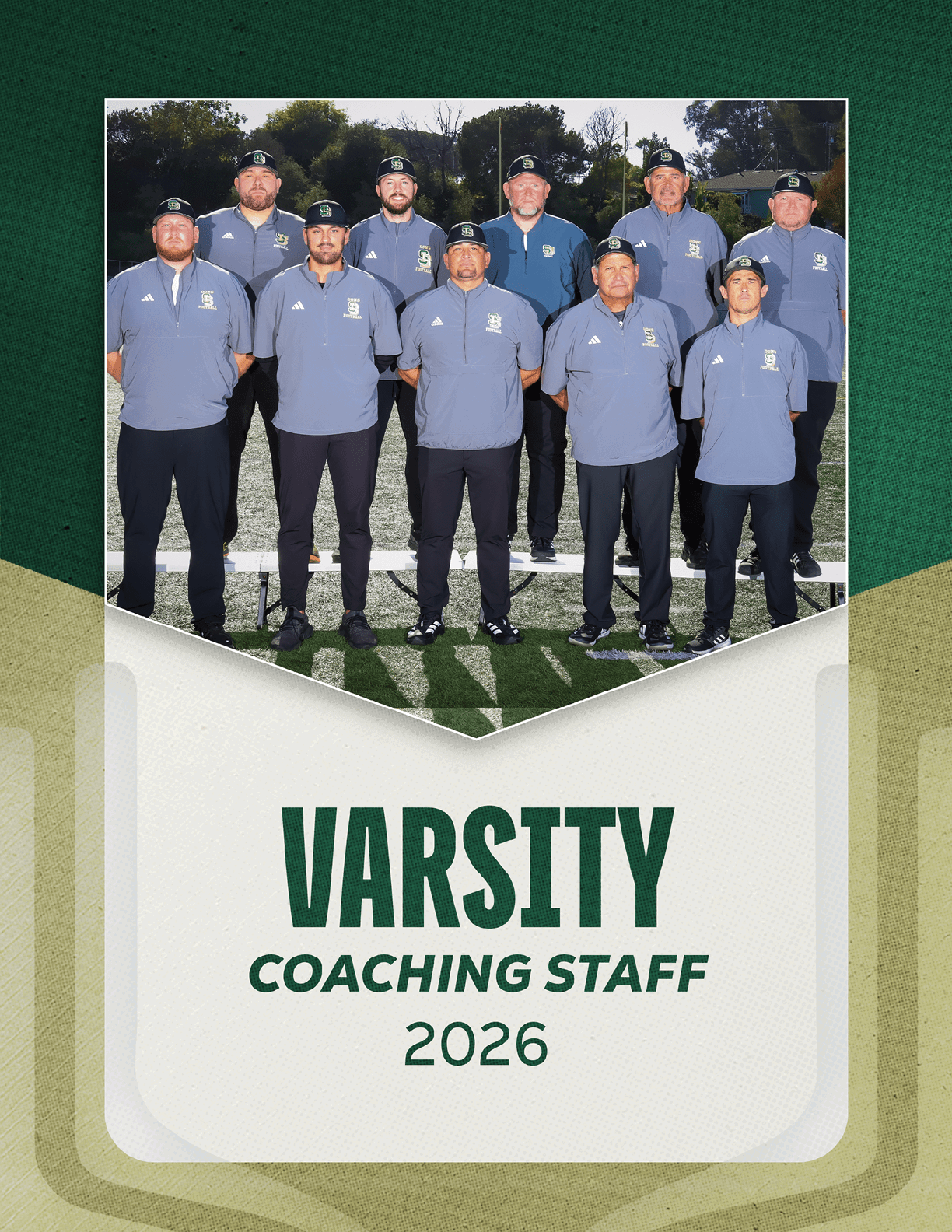 A group of nine adults wearing matching gray polo shirts and dark pants pose outdoors on a sports field with the text varsity coaching staff 2026 below them. Description generated by AI