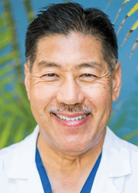 A person with short dark hair and a mustache is smiling warmly against a blurred background with green and blue tones. Description generated by AI
