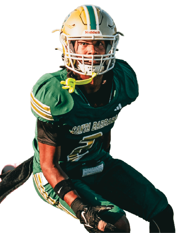 A person wearing a green and yellow football uniform and helmet is crouched in an athletic stance, appearing ready to play. Description generated by AI