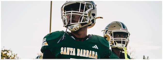 People wearing green football uniforms with “Santa Barbara" written on the jerseys are standing outdoors, appearing focused and ready for a game. Description generated by AI