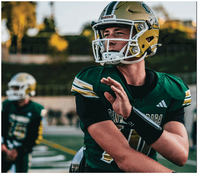 A person wearing a green and gold football uniform and helmet is preparing to throw a football on a field with another player in the background. Description generated by AI