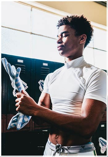A person wearing a white fitted shirt is putting on a padded sports glove in a locker room. Description generated by AI
