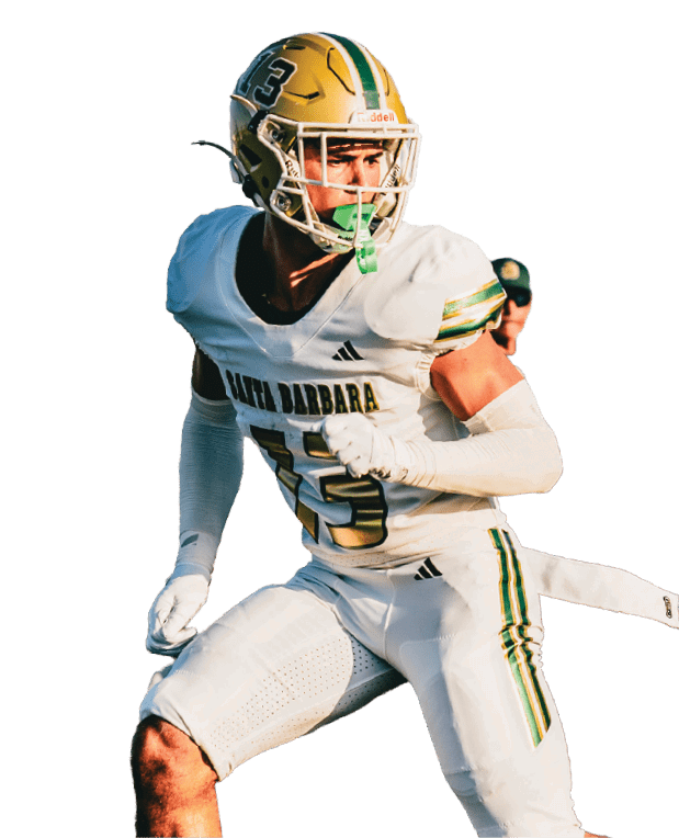 A person wearing a white football uniform with green and gold accents is in an action pose, holding a football. Description generated by AI