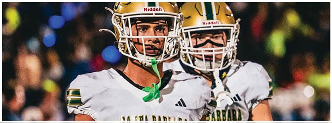 Two people wearing white sports jerseys with “Santa Barbara" and numbers 13 and 10 are standing close together, likely on a sports field. Description generated by AI
