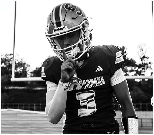 A person wearing a football uniform with the number three and the word Santa Barbara on the jersey is standing on a field with one hand near their mouth and the other hanging down. Description generated by AI