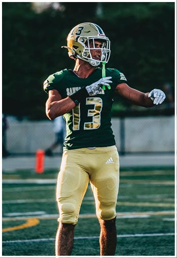 A person wearing a green and yellow football uniform with the number 13 is standing on a football field preparing to throw a ball. Description generated by AI